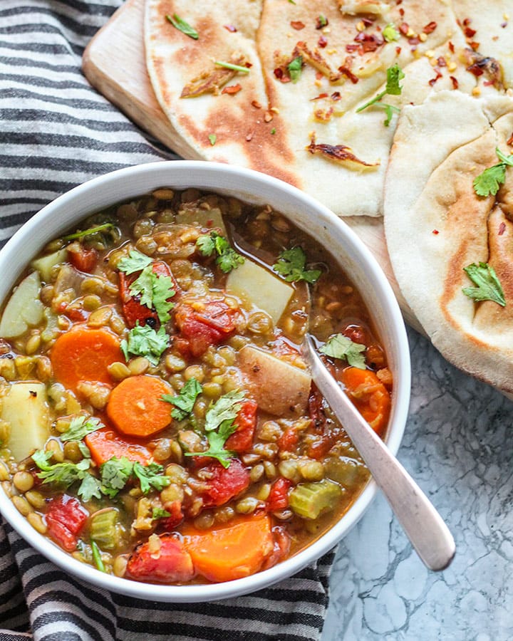 Bowl of lentil soup and veggies next to a plate of warm pita.