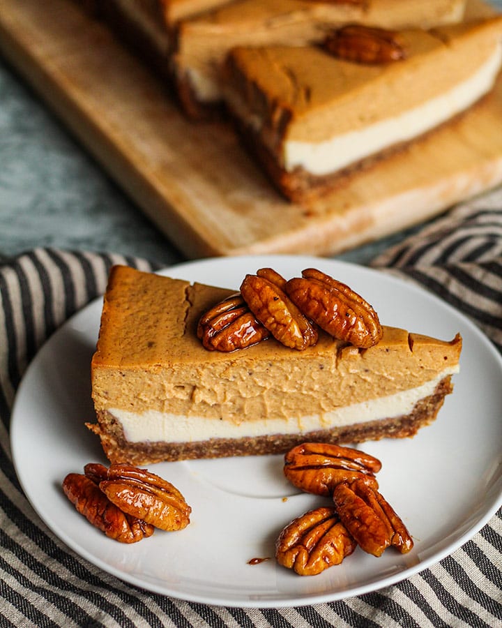 Slice of double layer pumpkin cheesecake sitting on a plate with candied pecans.