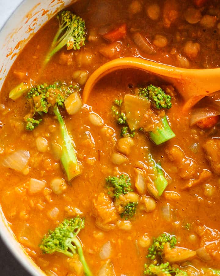 Stirring a large pot of pumpkin curry with broccoli.