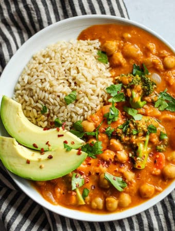 Pumpkin curry plated with a scoop of brown rice, avocado and some cilantro sprinkled over top.