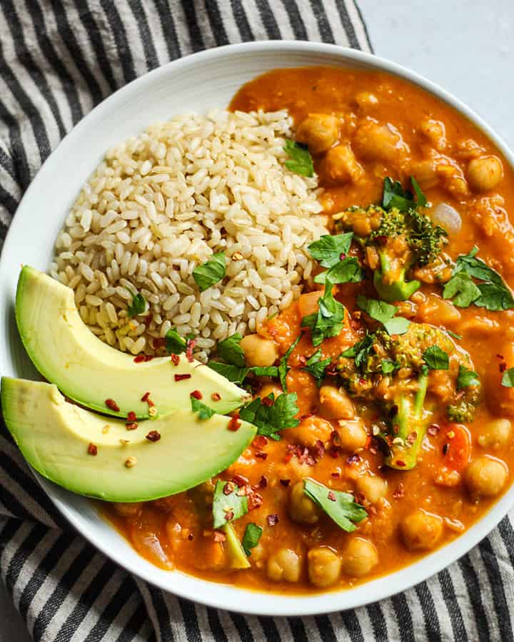 Pumpkin curry plated with a scoop of brown rice, avocado and some cilantro sprinkled over top.