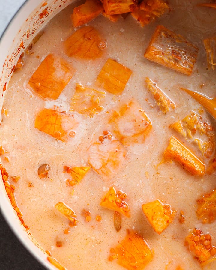 Large pot with coconut milk and vegetable broth mixed in with pumpkin and red lentils.