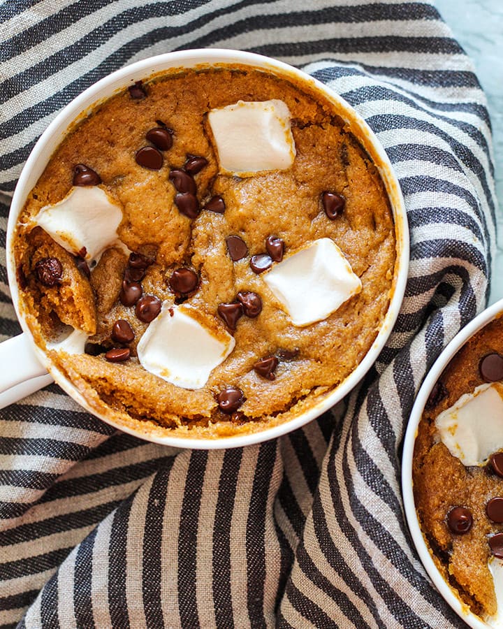 Two pumpkin mug cakes right out of the microwave with gooey chocolate chips and marshmallows on the surface.
