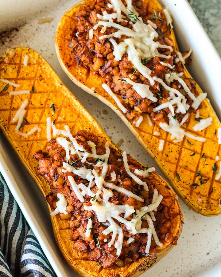 Two halves of stuffed butternut squash out of the oven with melted vegan cheese.