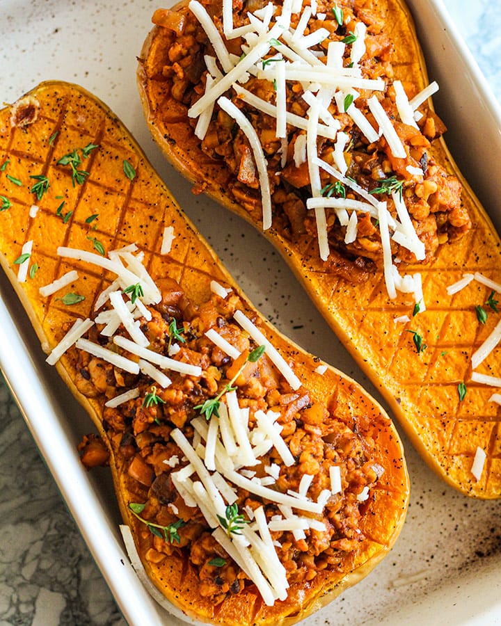 Butternut squash halves topped with minced tempeh and topped with thyme and vegan cheese.