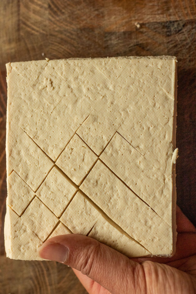 Cutting a shallow crosshatch on the tofu surface.