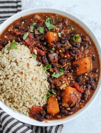 Plate of brown rice served with black bean and butternut squash stew topped with cilantro.