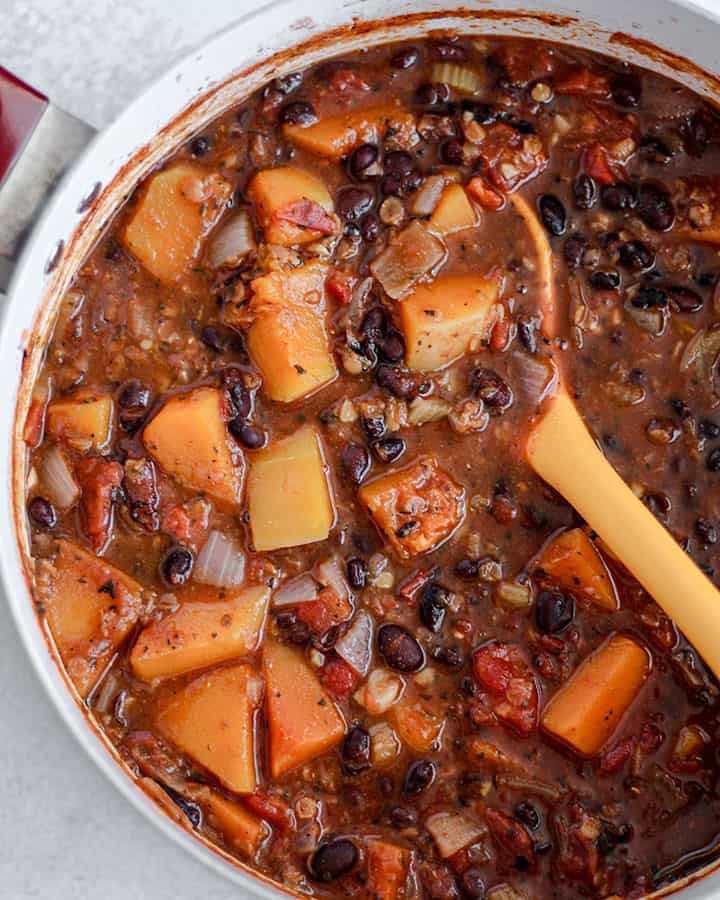 Black bean and butternut squash stew being stirred together in a large pot after cooking.