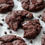 Side view of the tray of cookies with a scatter of chocolate chips around them. Middle cookie is pulled apart to show melted chocolate.