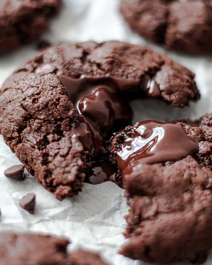 Close up of a cookie pulled apart from the center with chocolate overflowing where it has broken apart.