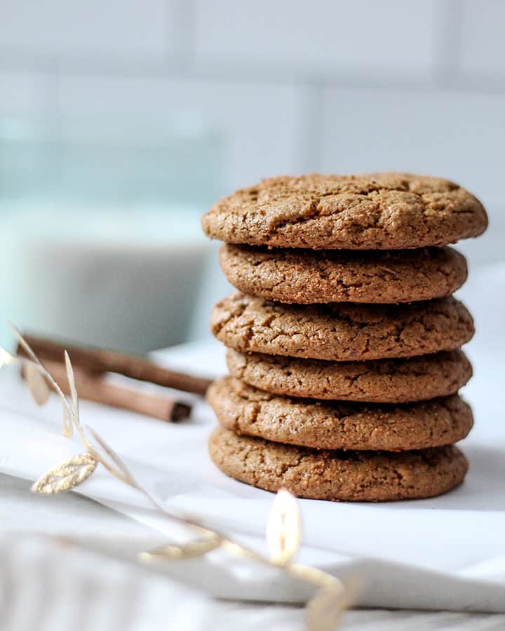 Stack of cookies to the side with cinnamon sticks and a glass of almond milk are faded in the background.
