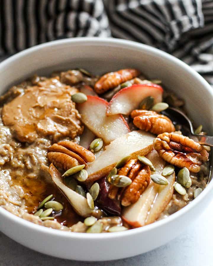 Tilted angle view of oatmeal loaded with sautéed pears, pecans, peanut butter and pepitas.