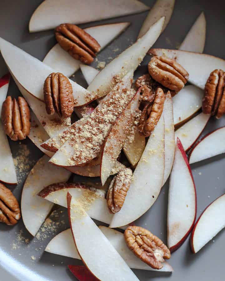 Sliced pears in a pan coated with ginger, cinnamon, pecans and maple syrup.