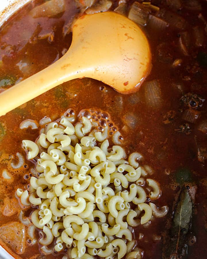 Adding macaroni in to cook in the rich tomato broth.