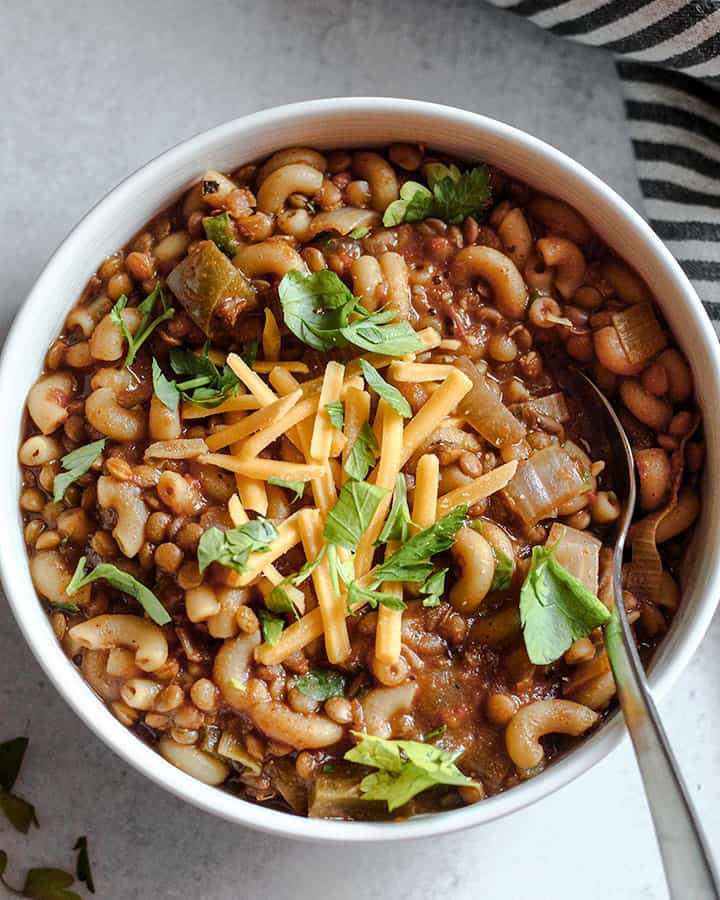 A warm bowl of lentil and tomato macaroni soup topped with vegan cheese and fresh minced parsley.