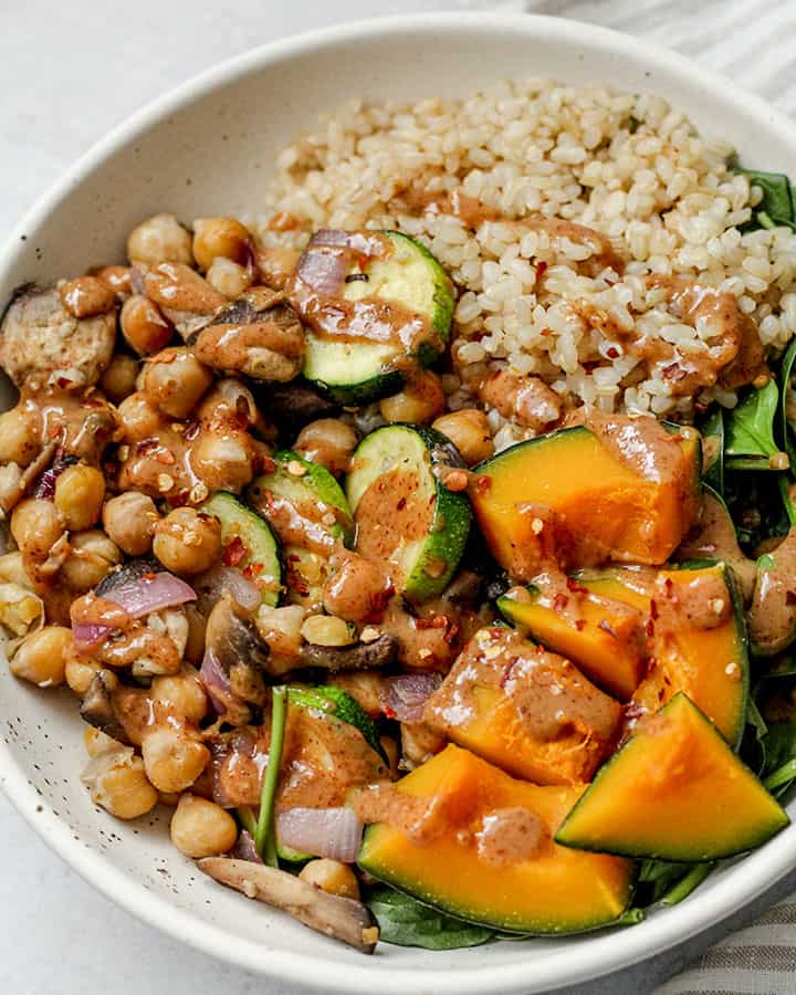 Side view of sautéed chickpeas and vegetables with brown rice and almond miso sauce poured overtop.
