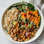 Bowl of veggies, grains, beans and squash, topped with sauce and sliced scallions.