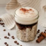 Jar of overnight oats with towel in the background and coffee beans and cinnamon sticks.