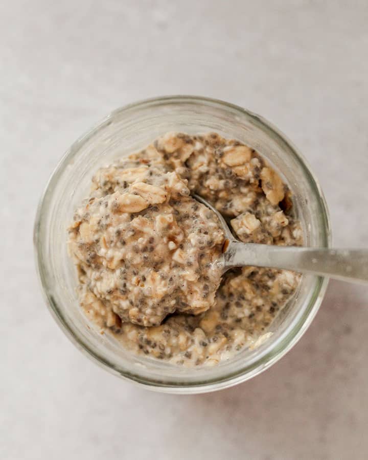 Oats fully gelled after sitting in the fridge overnight. Oats are in a open jar being mixed around with a silver matte spoon.