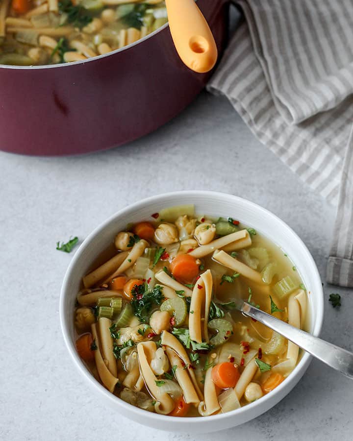 Soup in a white bowl with a spoon for serving set next to a background image of the pot of soup after serving.