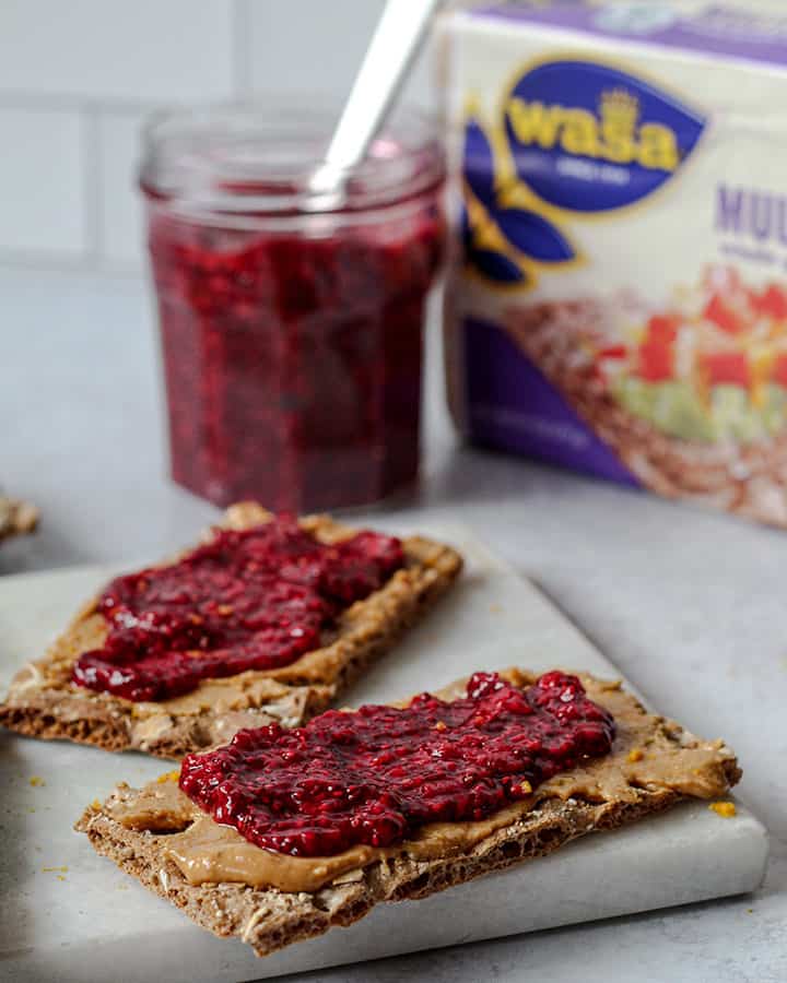 Crispbread snacks with jam and nut butter up front with jar of freshly made jam and extra crispbreads in the back.