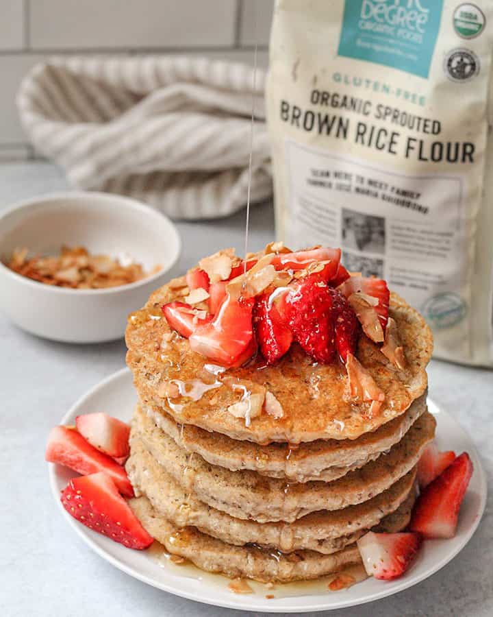 Stack of pancakes topped with coconut flakes, strawberries and syrup.