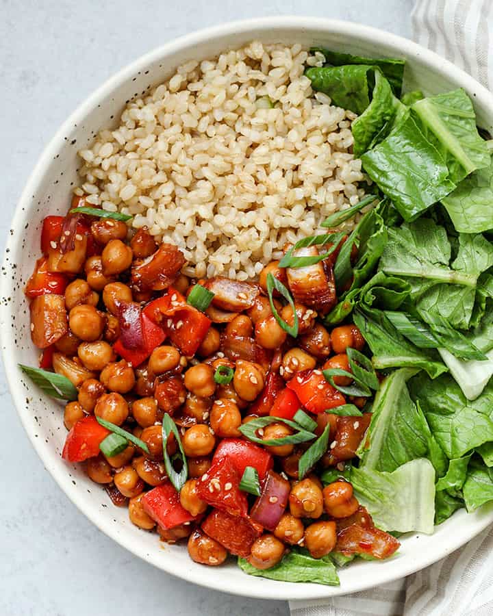 Top down view of a bowl of glossy chickpeas paired with brown rice and lettuce.