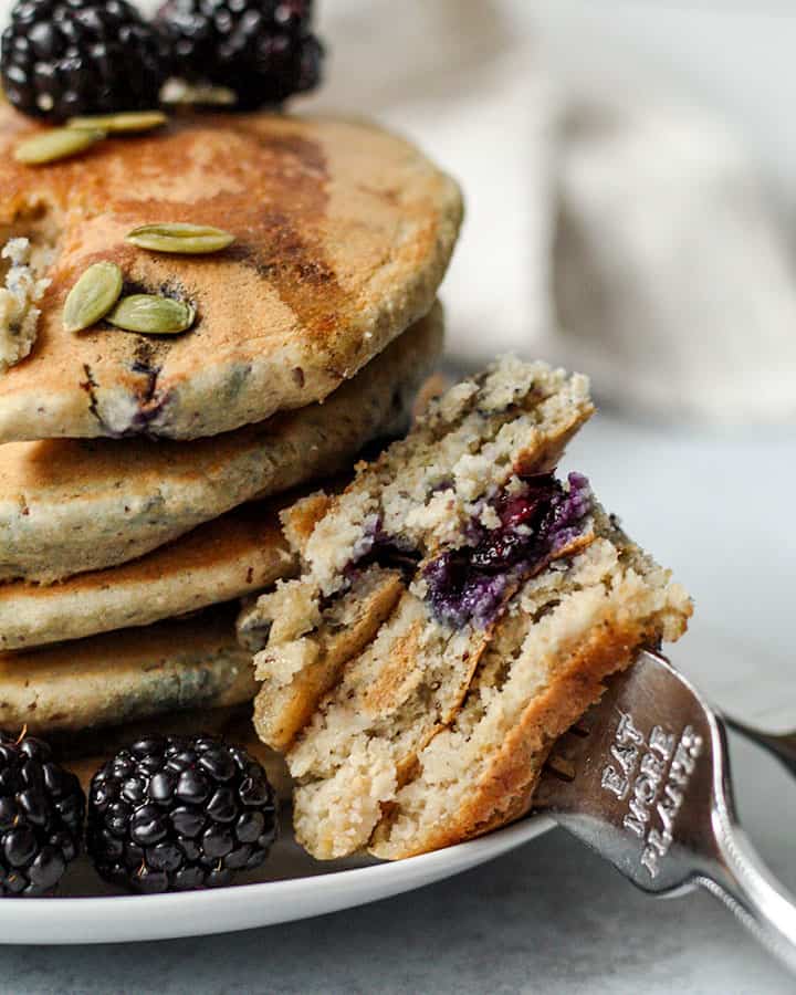 A forkful of blueberry pancakes resting by a plate of stacked pancakes.