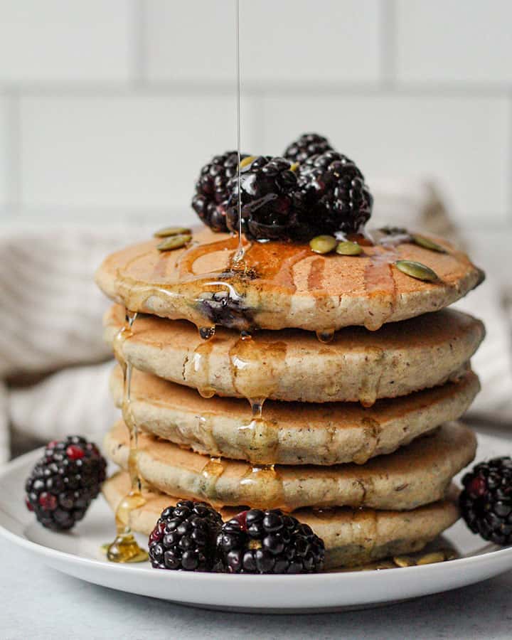 A stack of blueberry pancakes topped with blackberries and drizzled with maple syrup.
