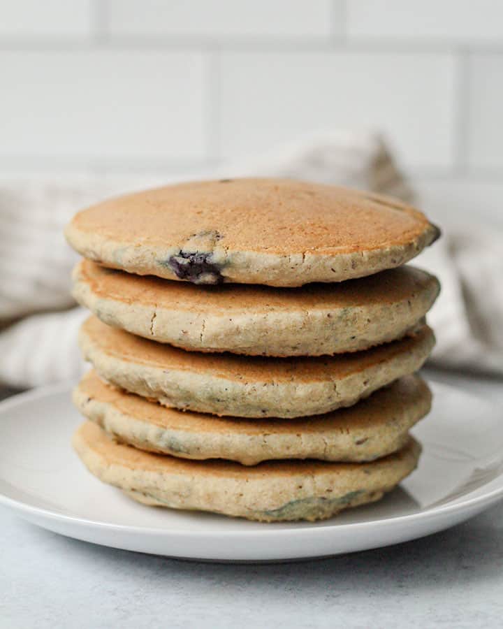 A stack of fluffy pancakes sitting on a white plate with a striped napkin in the background.