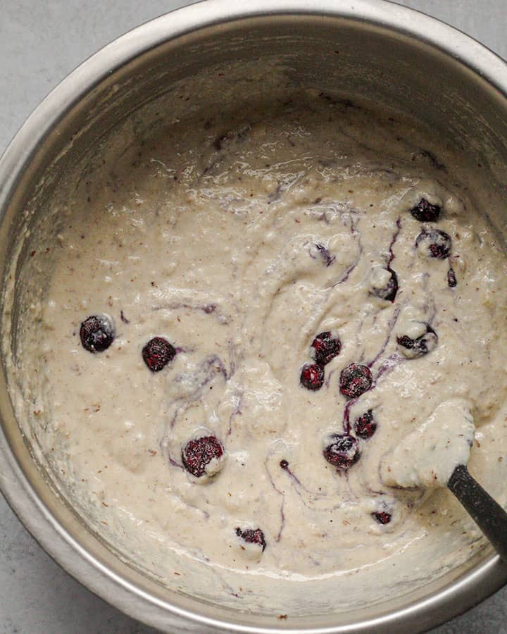 Full pancake batter with blueberries folded in with a spatula in a metal mixing bowl.