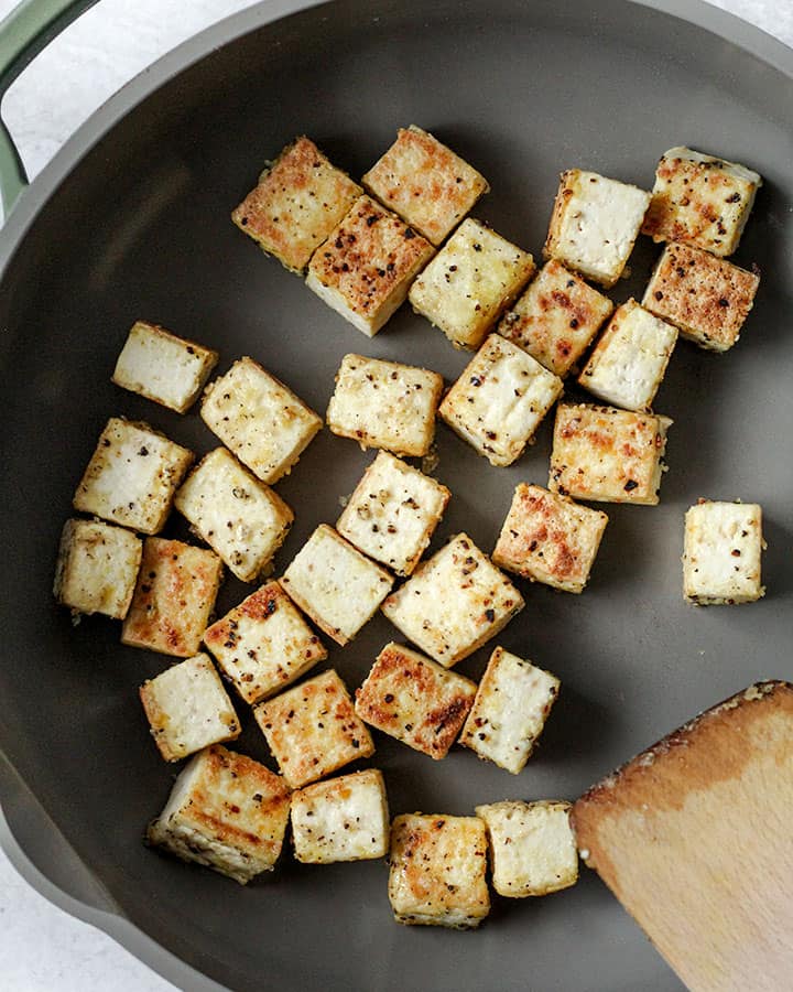 Golden coated and seasoned tofu being toasted in a pan on all sides.