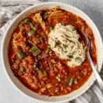 Giant white bowl of lasagna soup with vegan ricotta to top with and a spoon tucked into the side.