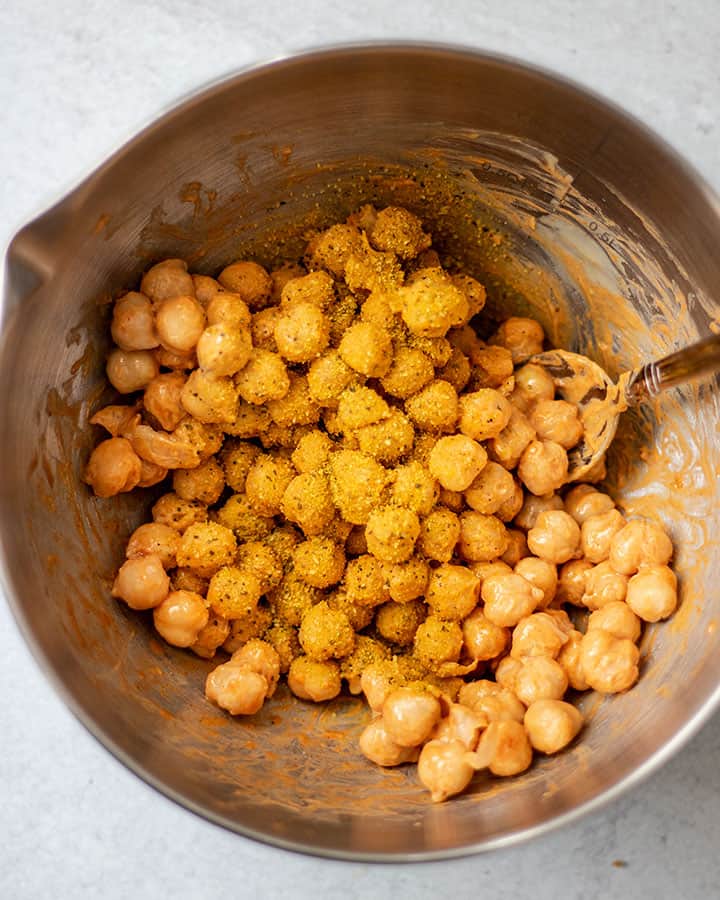 Chickpeas in a mixing bowl being coated wtih tahini, paprika and adobo seasoning.