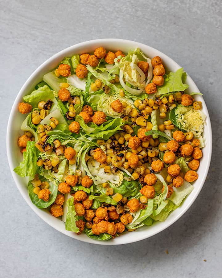 Bowl with greens topped with chickpeas and fire roasted corn.