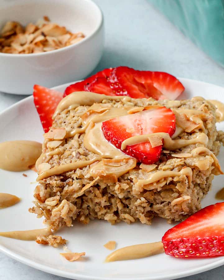 A plate of a fresh square cut of baked oatmeal served with sauce and strawberries.