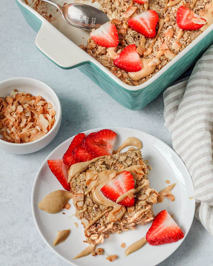 A single serve slice of baked oatmeal served with extra strawberries, sauce and toasted coconut.