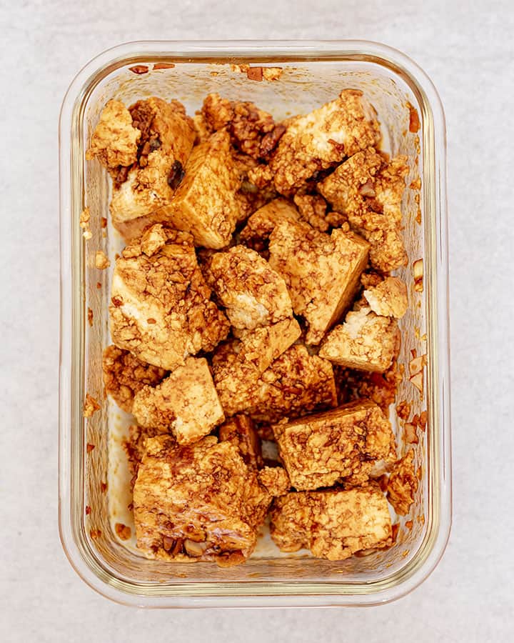 Tofu tossed with sauce in a glass container.