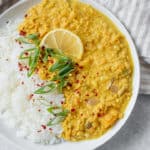 Plate of white Jasmine rice with curry served on the side garnished with scallions, red pepper flakes and a wedge of lemon.