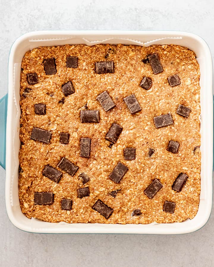 The dough mixture spread out evenly in a square baking dish and covered with extra chocolate chips.