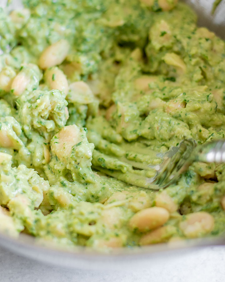 Bowl of white beans being mixed and mashed with pesto.