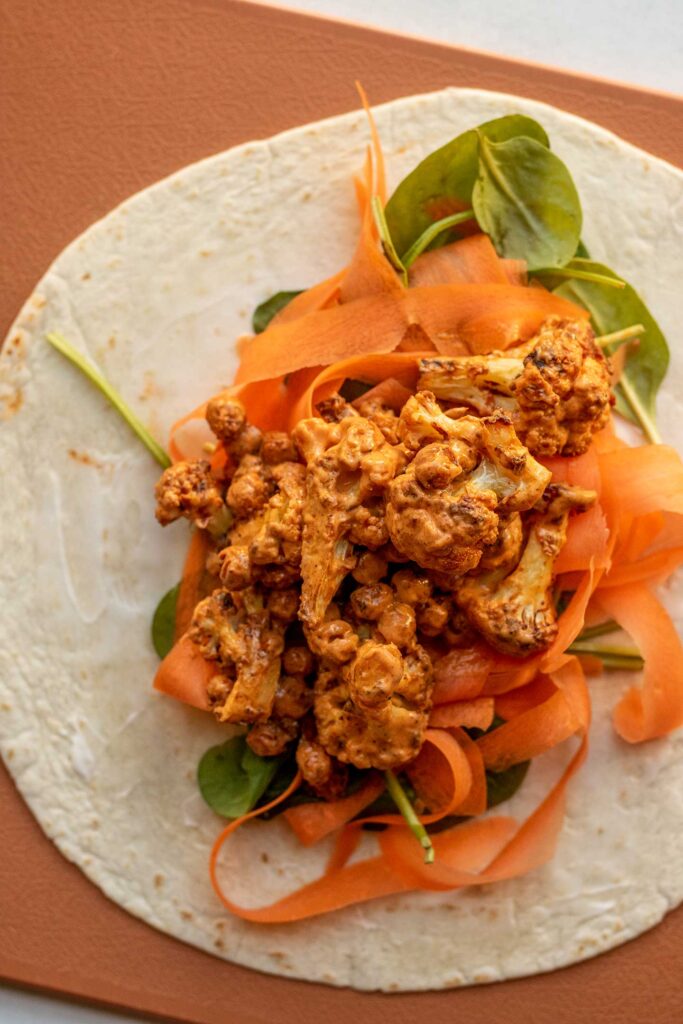 A flour tortilla layered with spinach, shredded carrots and the buffalo chickpea cauliflower filling on top.