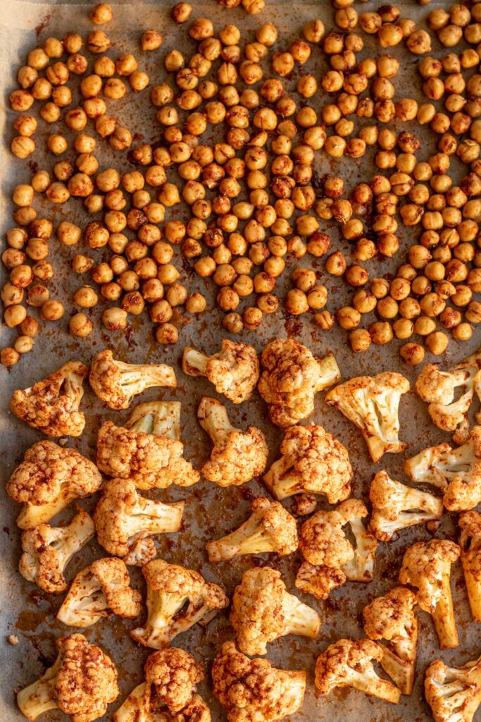 Chickpeas and cauliflower seasoned with spices and spread out evenly on a parchment lined baking tray.
