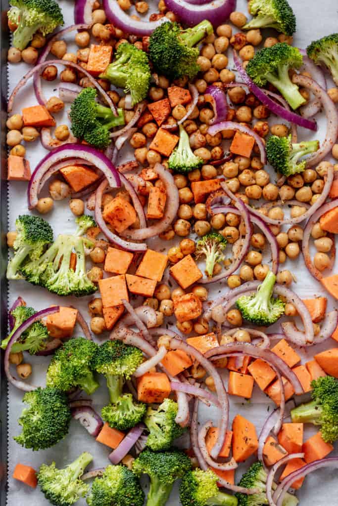 Sheet pan covered with diced sweet potato, broccoli, onions and chickpeas covered in herbs and spices ready to bake.
