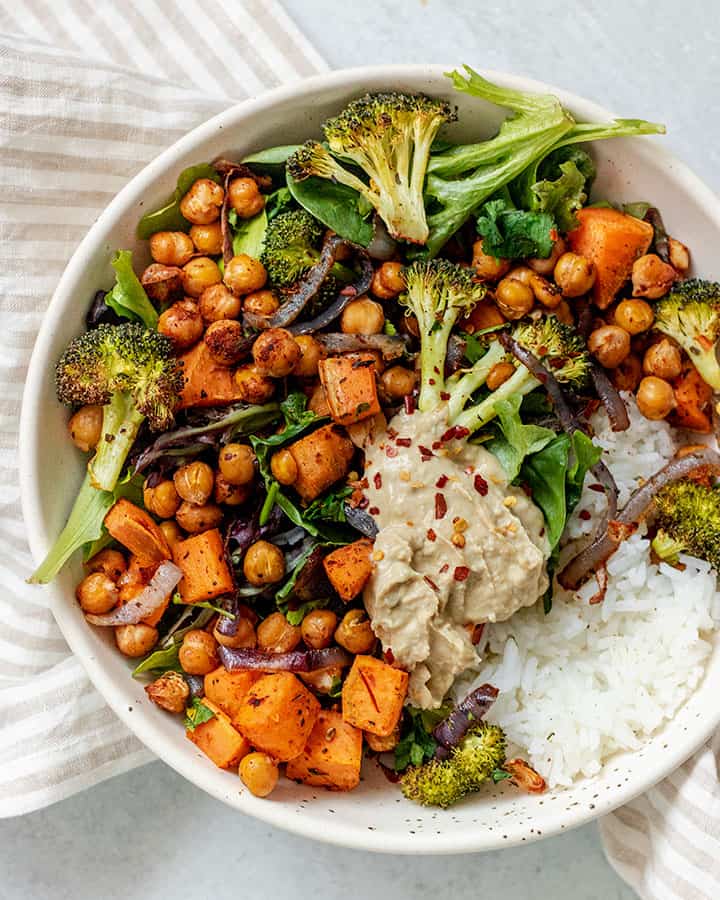 White bowl filled with rice topped with roasted chickpeas, broccoli and sweet potato.