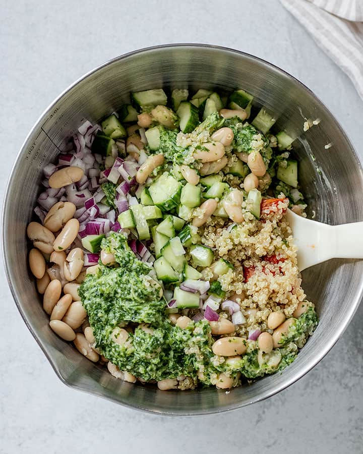 Quinoa, vegetables and beans topped with dressing in the process of being mixed in a bowl.