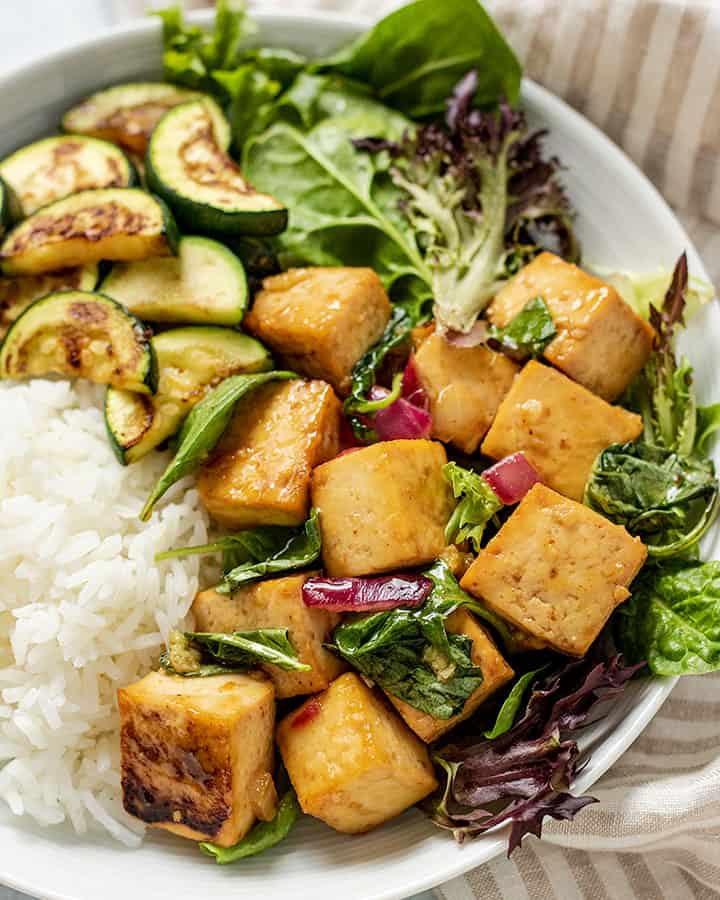 Plate of tofu paired with zucchini, spring greens, and white rice.