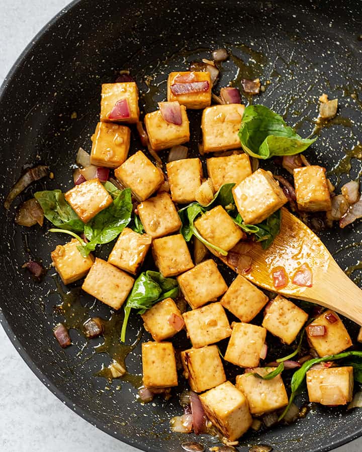 Tofu being mixed with fresh basil in a sauté pan.