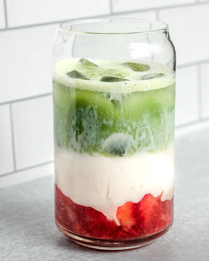 Glass of mashed strawberries, milk and matcha with ice.
