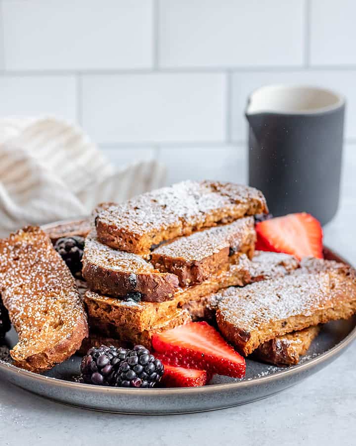 Plate of French toast sticks dusted with powdered sugar and surrounded by sliced berries.